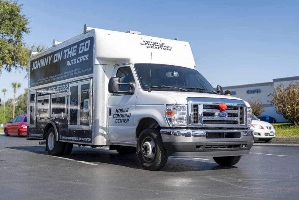 A white Ford commercial food service truck is parked in a sunny outdoor lot, equipped for mobile catering or food service operations.