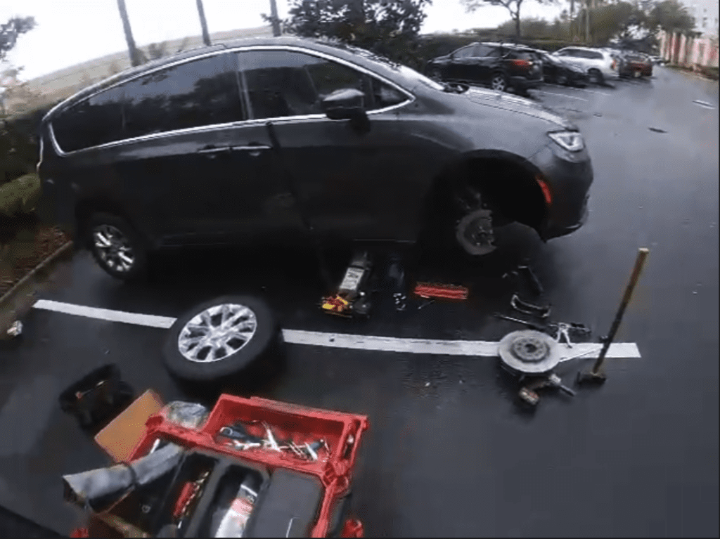 An overhead view of a black SUV elevated on a car lift in a parking lot with automotive tools and equipment spread below it.