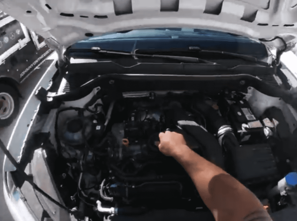 A person inspects or works on a car engine under the open hood in daylight.