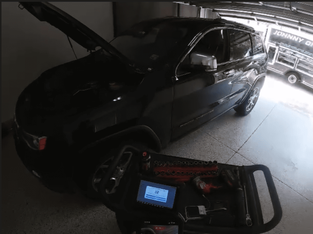 A black pickup truck is parked in an indoor workshop or garage while a diagnostic scanner device sits on the floor in front of it.