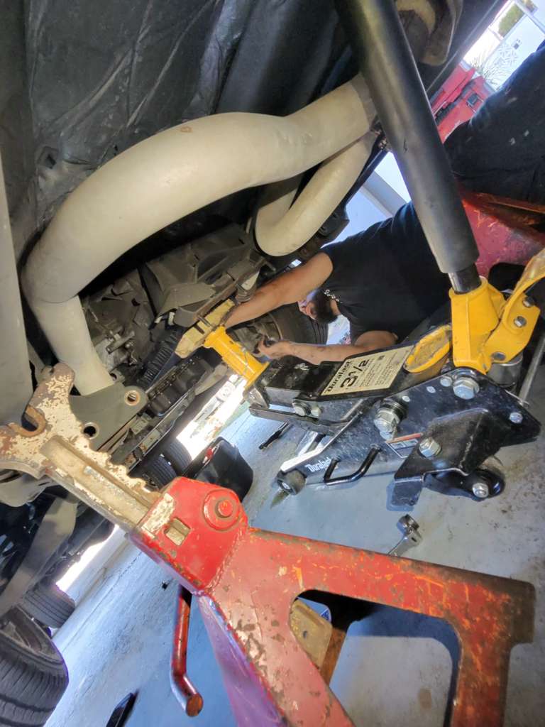 An overhead view of a cluttered workshop or garage floor with various power tools, hand tools, and equipment organized on a red work surface.