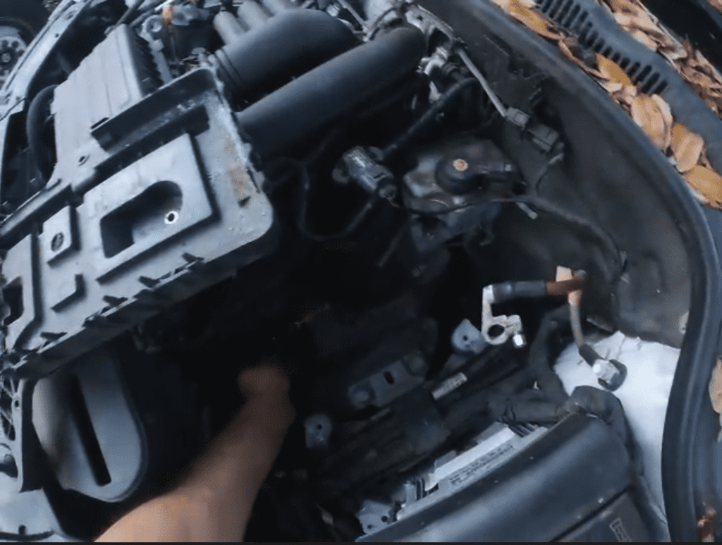 A mechanic wearing gloves works on an engine in a vehicle's engine compartment during daytime.