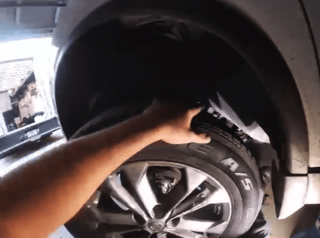 A mechanic works on a vehicle tire or wheel in a workshop setting, captured in close-up during hands-on automotive maintenance.