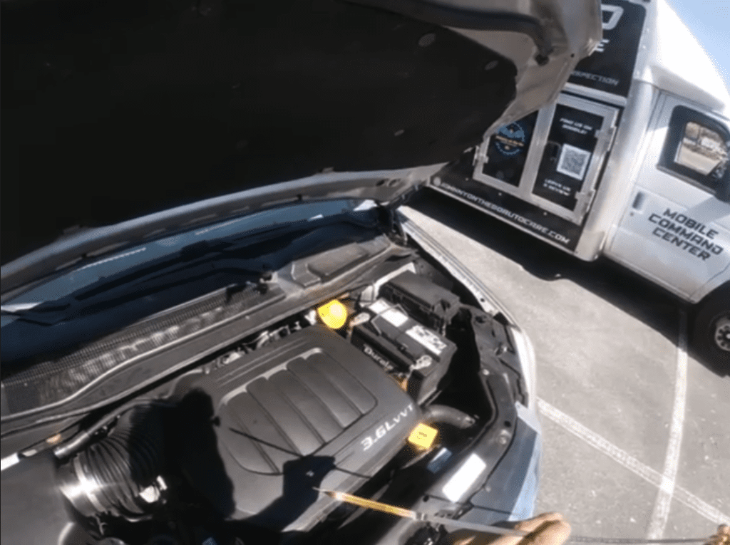 A close-up view of an open car hood revealing the engine compartment with visible engine block and mechanical components.