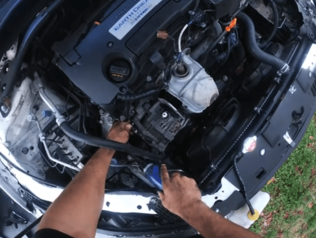 A mechanic's hands work on an engine block during vehicle maintenance or repair in bright daylight.