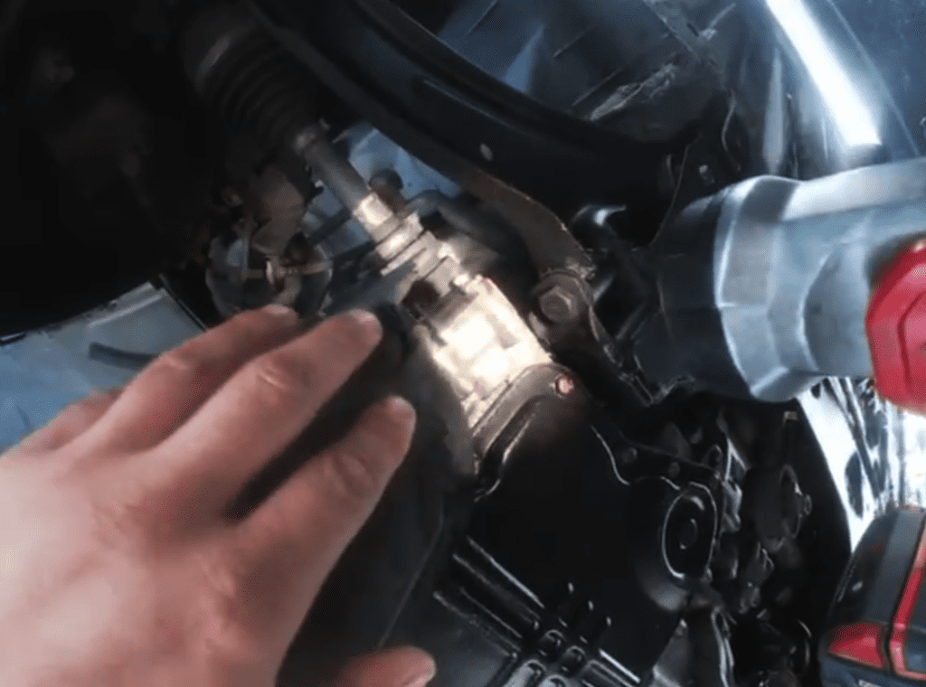 A close-up view of a person's hand examining or working on a motorcycle engine with visible metallic components and chrome details in an indoor workshop setting.