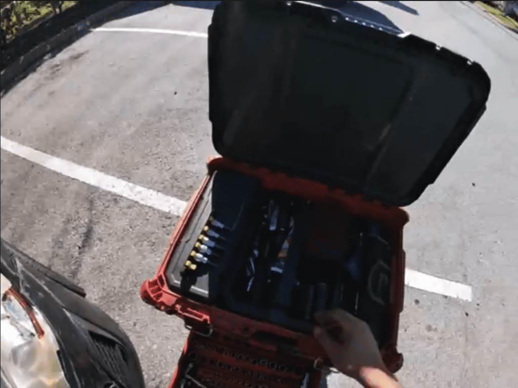An overhead view of an open black tool bag with red straps sitting on a parking lot with white line markings.