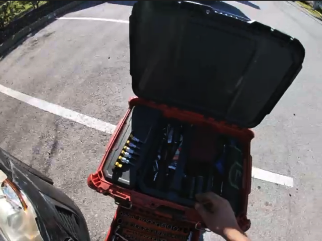 An overhead view of an open black tool bag with red straps sitting on a parking lot with white line markings.