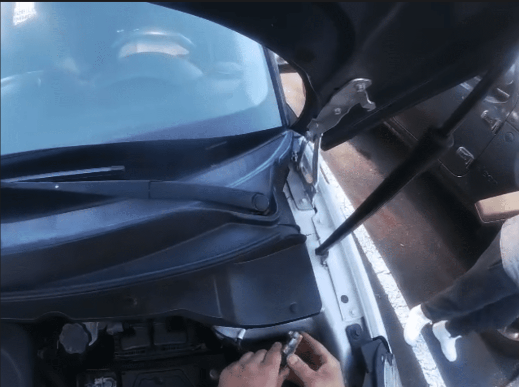 A close-up shot of someone opening a car door in daylight, showing the windshield and blue sky in the background.