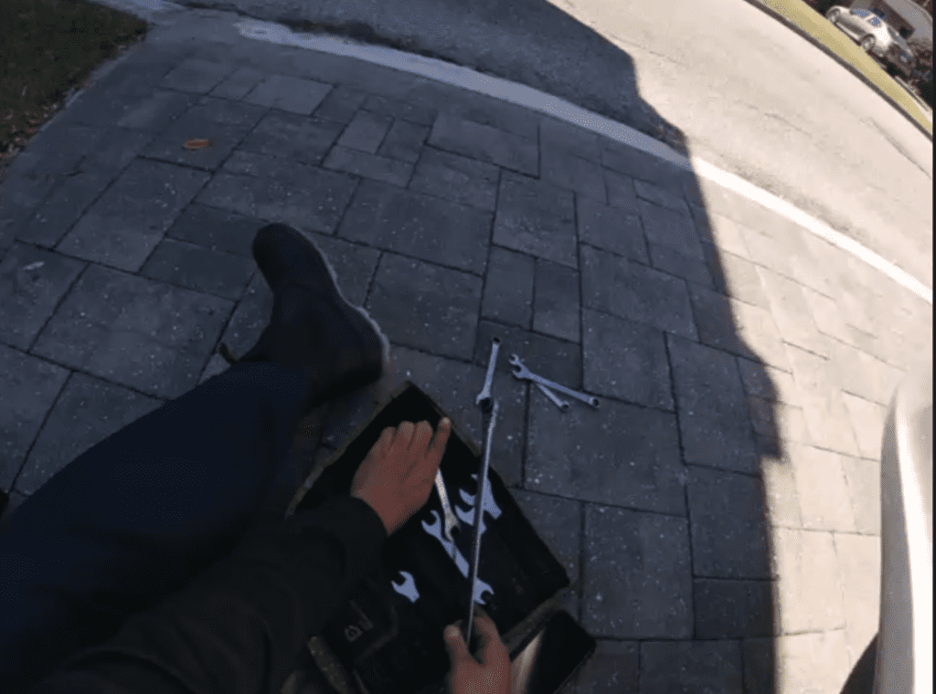 A person's shadow cast on pavement holding what appears to be a rifle or long gun, shot from above.
