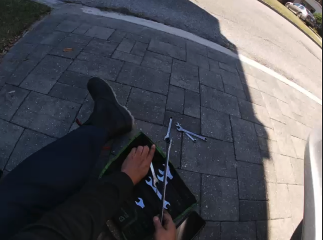 A person's shadow cast on pavement holding what appears to be a rifle or long gun, shot from above.