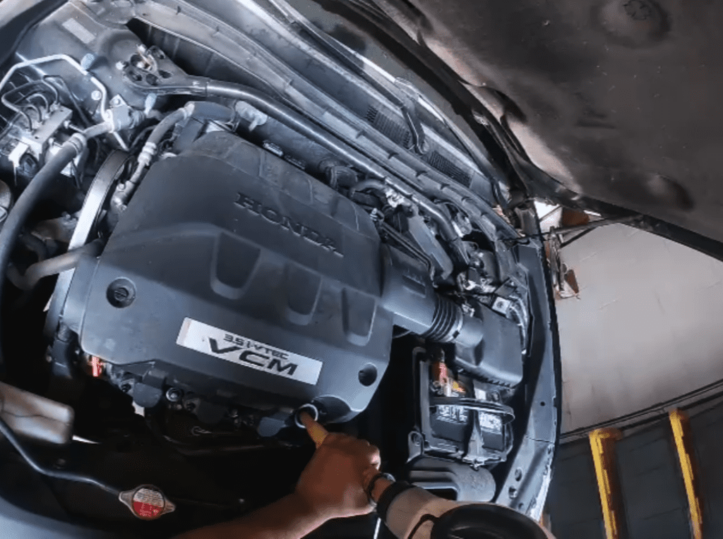 A close-up view of a V8 car engine with visible engine block, intake manifold, and engine cover showing mechanical detail and industrial design.