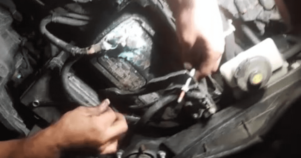 A mechanic's hands work on disassembling or repairing an engine block using hand tools in a workshop setting.