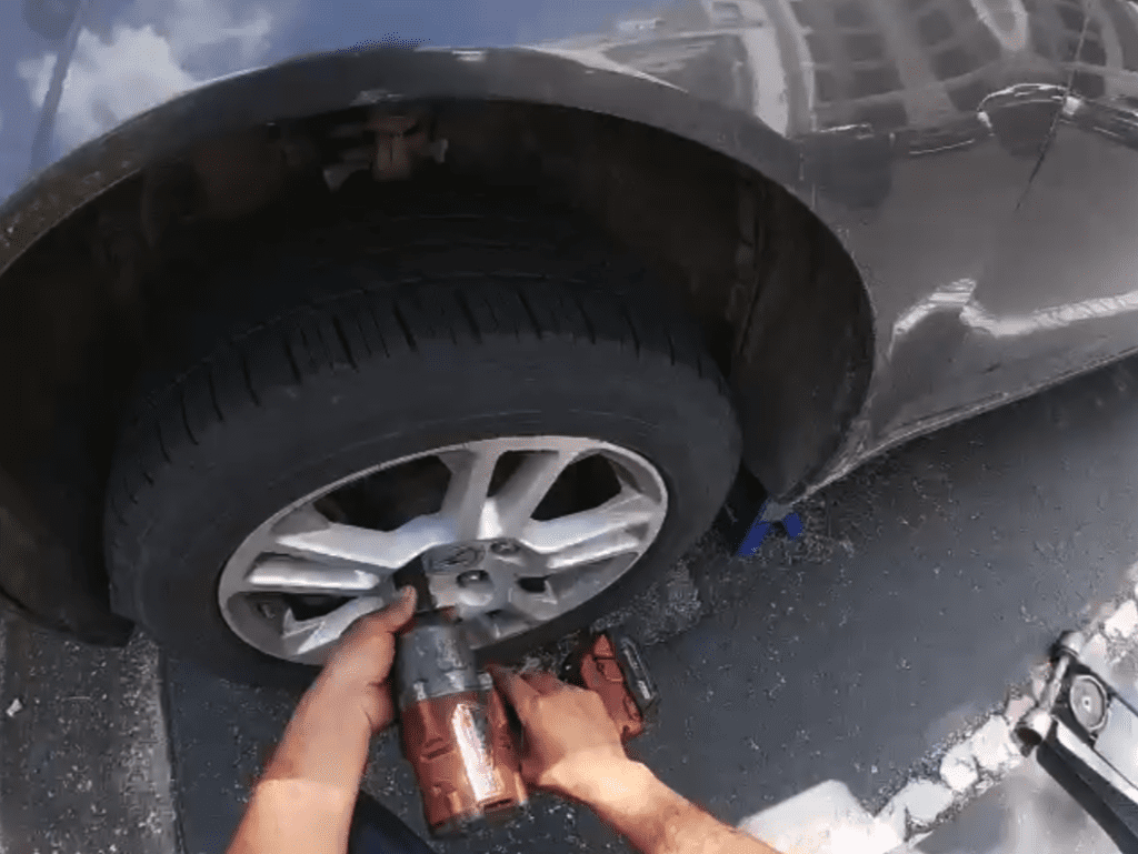 A mechanic's hands work on removing or installing a tire on an alloy wheel during outdoor roadside repair work.