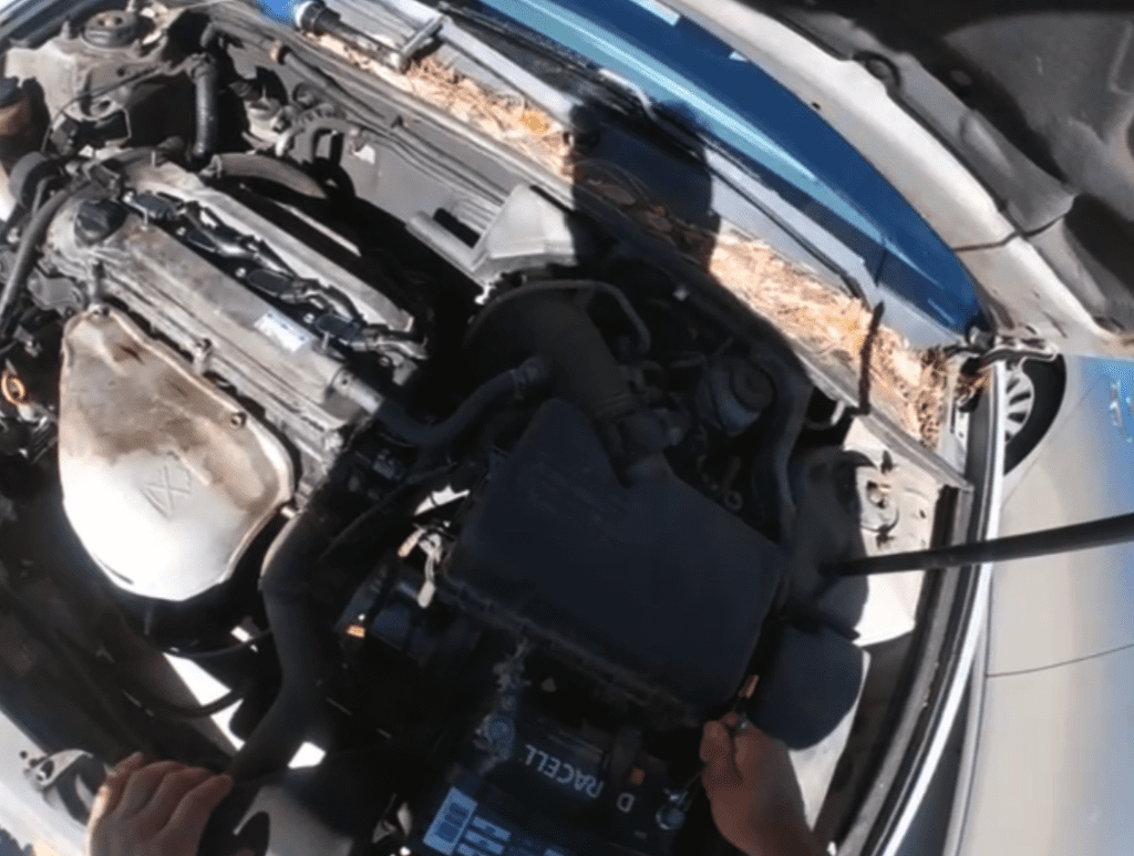 A mechanic works on an engine in an overhead view, performing maintenance or repair work on what appears to be a blue vehicle.