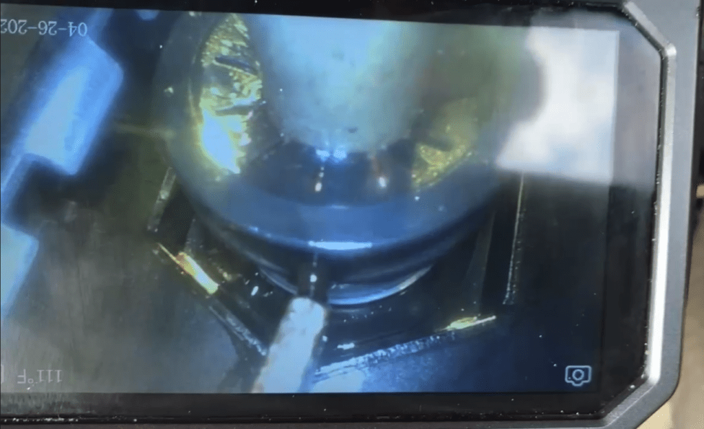 Close-up view of industrial machinery or mechanical equipment with blue metallic components captured on a surveillance or workshop camera feed.