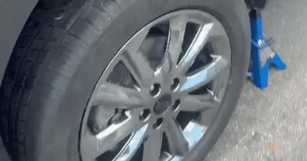 A close-up view of a car wheel being lifted with a blue jack during a tire maintenance or replacement procedure.