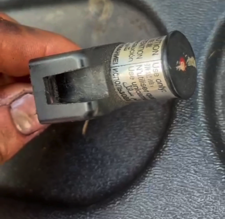 A close-up shot of a person's hand holding a vehicle seatbelt connector against a gray fabric car seat.