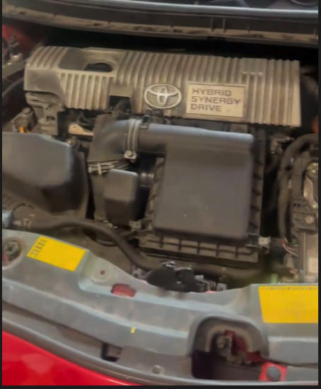 A close-up view of a vehicle's engine bay showing the air filter box and engine cover with yellow warning indicators visible.