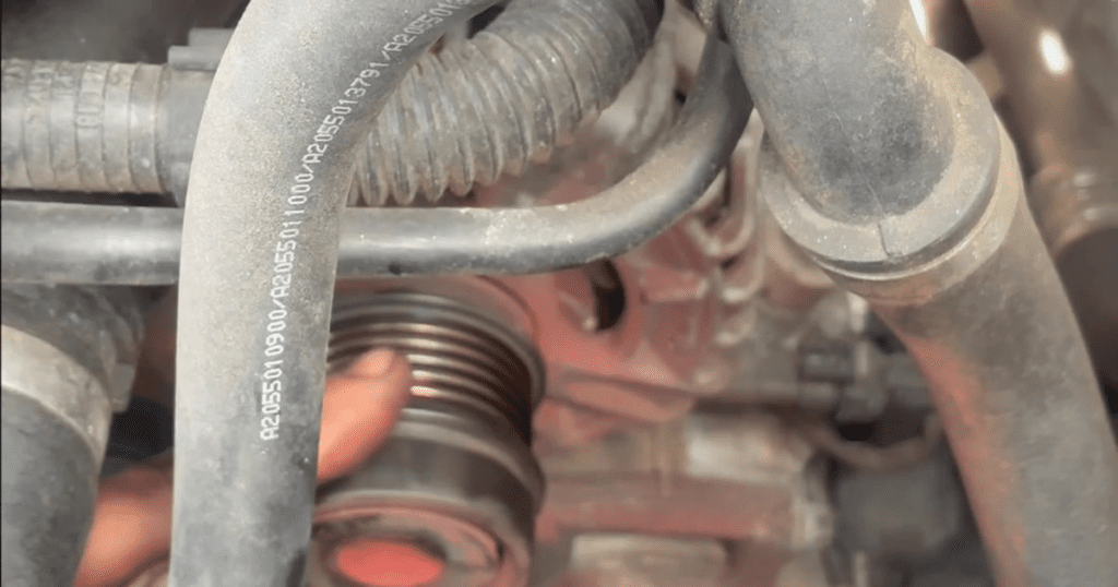 A close-up view of an engine component showing a red coil with attached hoses and metal fittings in a workshop setting.