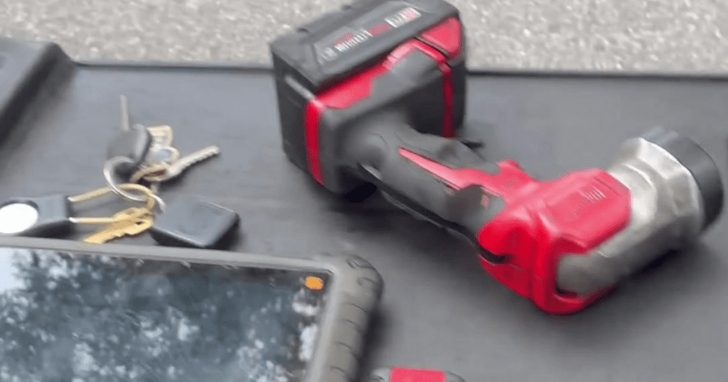 Red and gray adjustable dumbbells and a red toolbox arranged on a concrete workshop surface.