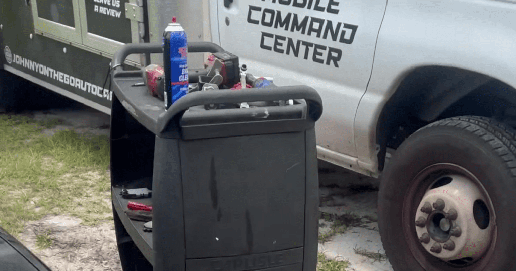 A person stands near a black command center trailer at an outdoor venue, likely part of an event management operation.
