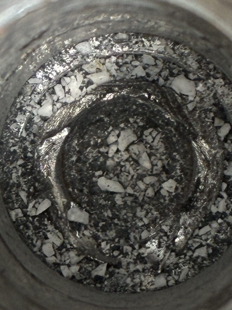 An overhead view of a metal mixing bowl containing dark batter or dough mixed with white flour or powdered ingredients during food preparation.