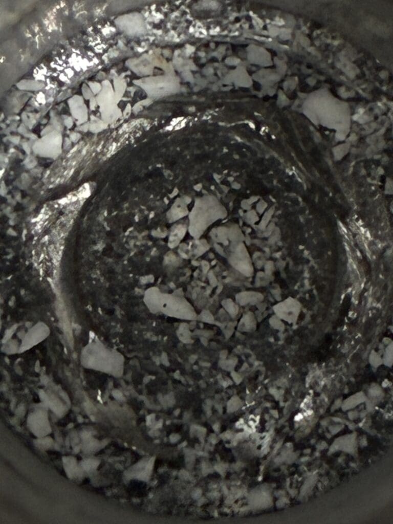 An overhead view of a pot or bowl containing a dark mixture with white granules or chunks, showing active cooking or food preparation in progress.