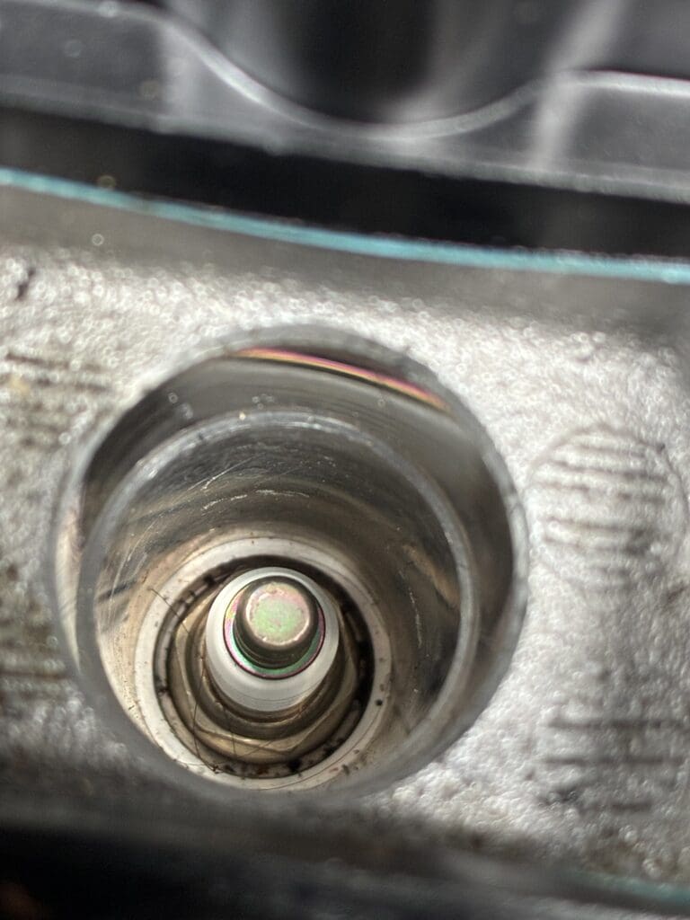 A close-up photograph of a metal threaded fastener or bolt mounted on a gray metallic surface.