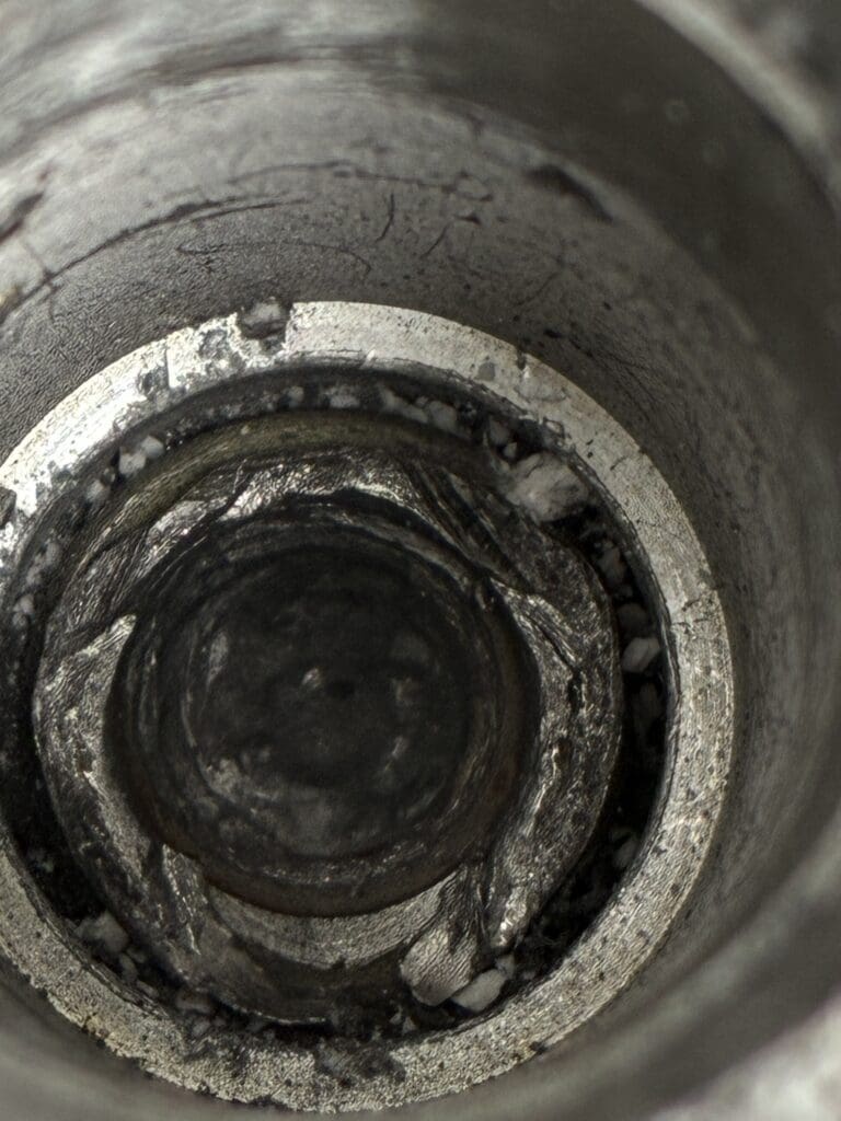 A close-up overhead view of the interior of a concrete or metal pipe showing mineral deposits and buildup around the circular opening.