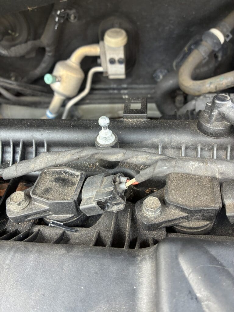 A close-up view of automotive engine components showing hoses, wiring, and mechanical parts in an engine bay.