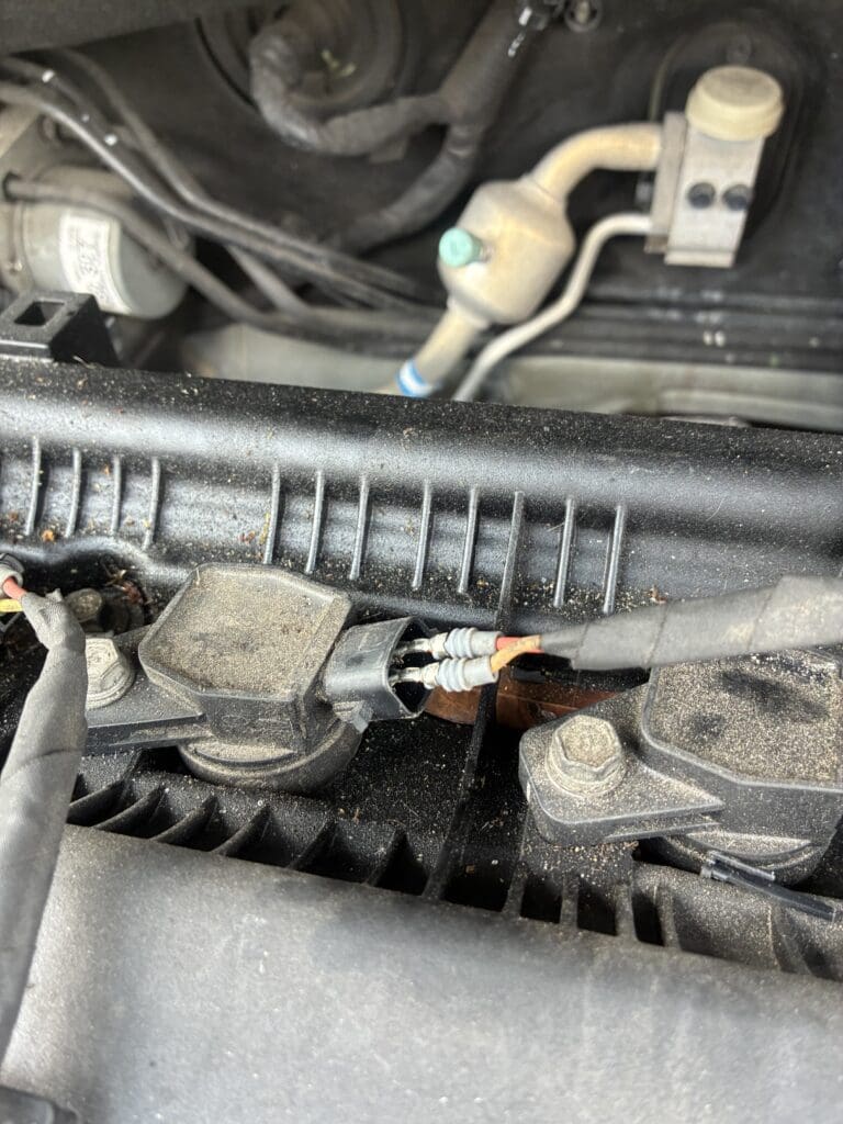 A close-up view of an engine bay showing fluid reservoirs, hoses, and various mechanical components in typical workshop lighting.