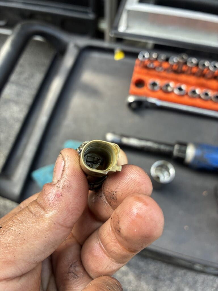 A close-up of a brass plumbing fitting being held in a worker's hand over a workshop tool organizer.