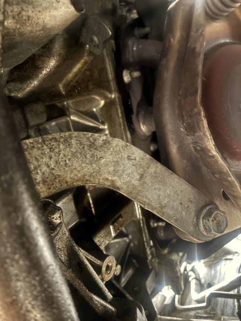A close-up view of a vehicle's brake caliper and rotor assembly showing mechanical wear and metal components in a workshop setting.