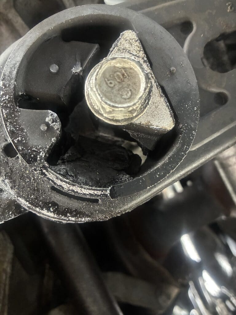A close-up overhead view of a metallic bolt with a hexagonal nut threaded onto it, covered in dust or powder residue, mounted in a dark mechanical assembly.